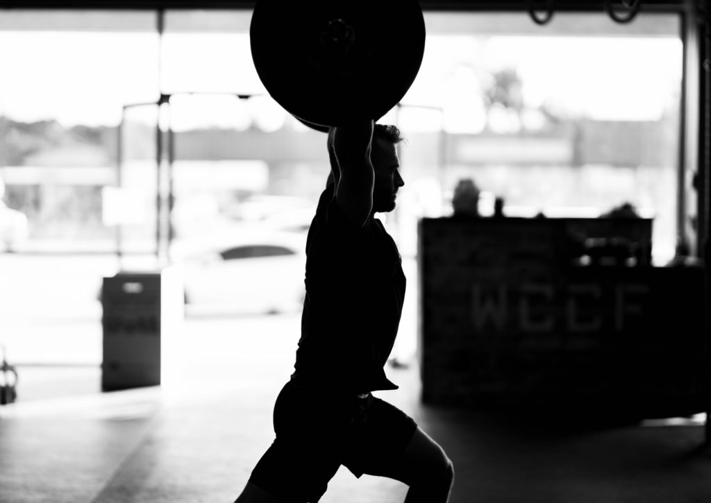 silhouette of man doing split jerk in gym
