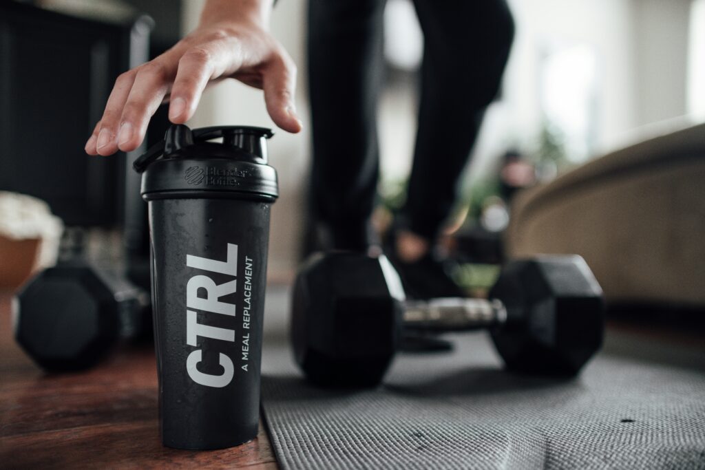 woman reaching for protein shaker bottle on gym floor