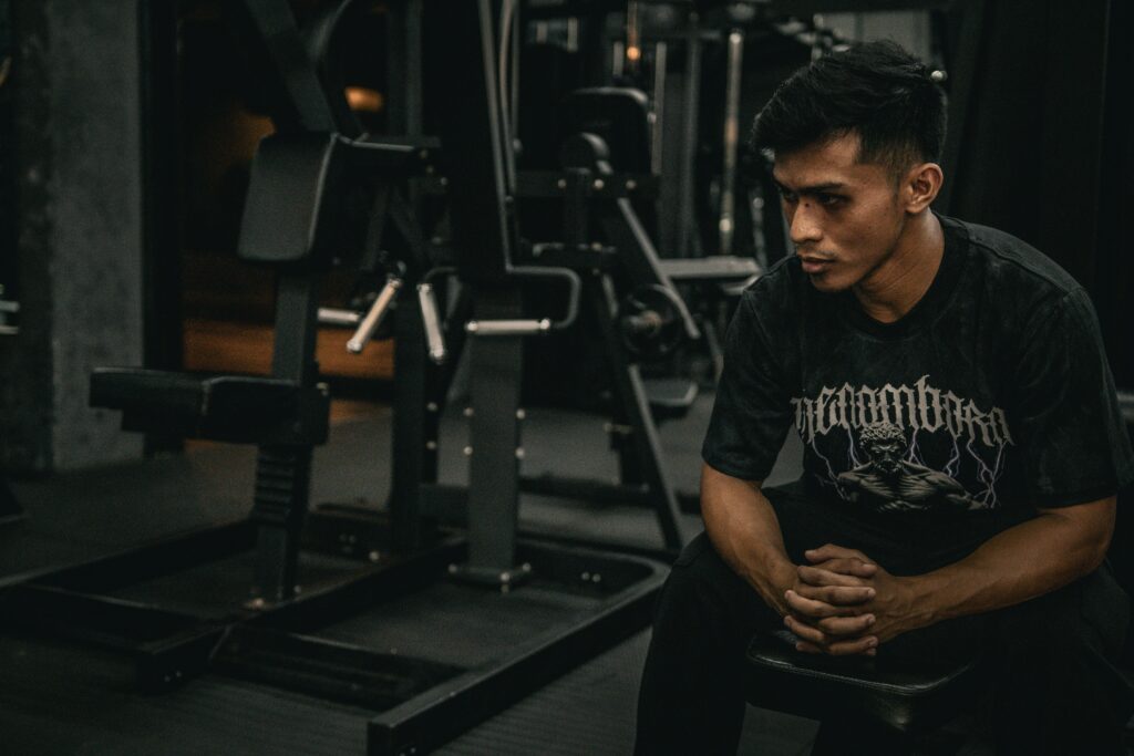 man sitting on bench in gym between sets