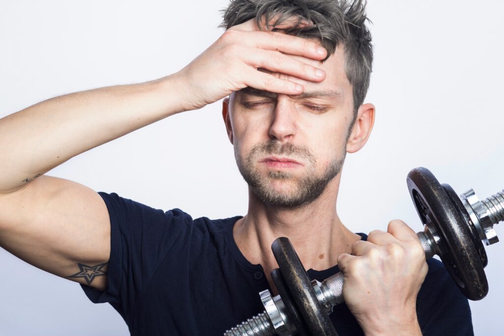 close up of man looking not motivated to exercise, holding dumbbell with one hand and his forehead with another