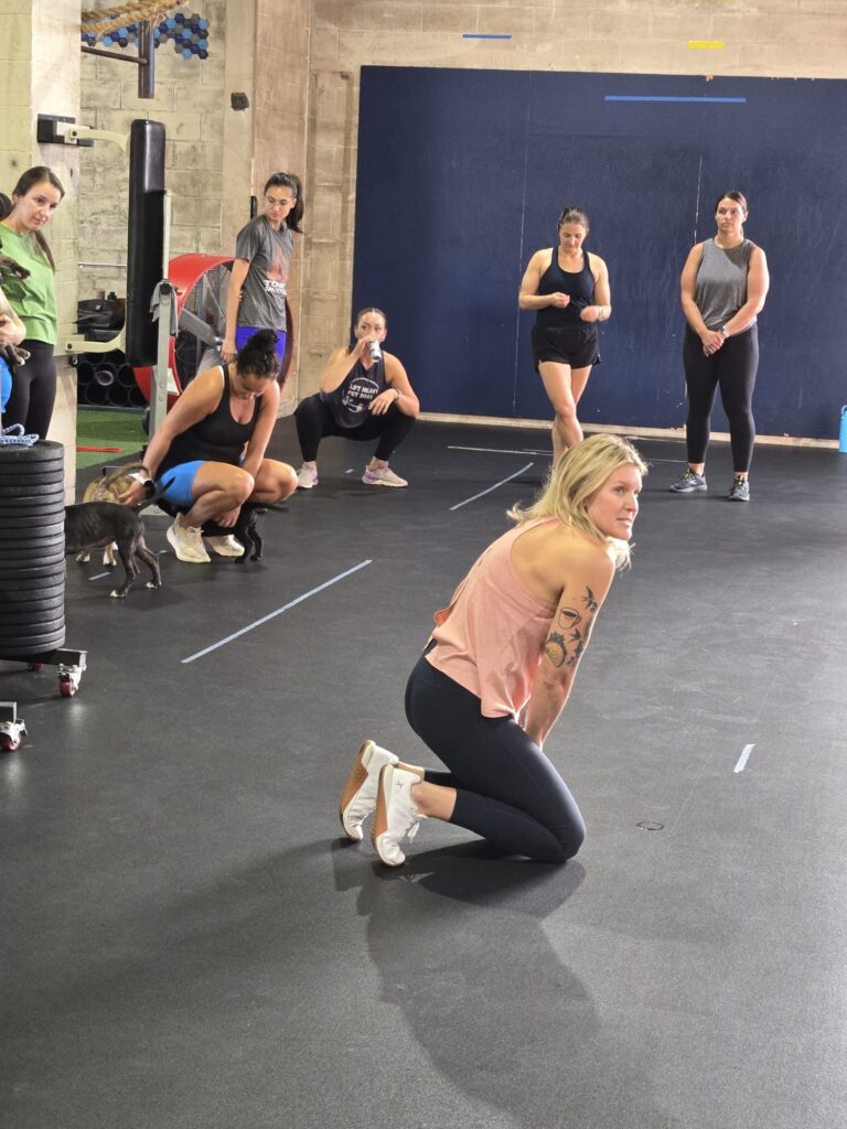 female coach kneeling on floor of gym while talking to group of athletes
