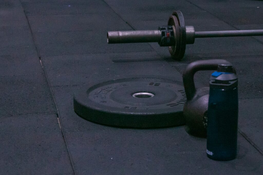close up of a barbell, bumper plate4, kettlebell, and water bottle on gym floor